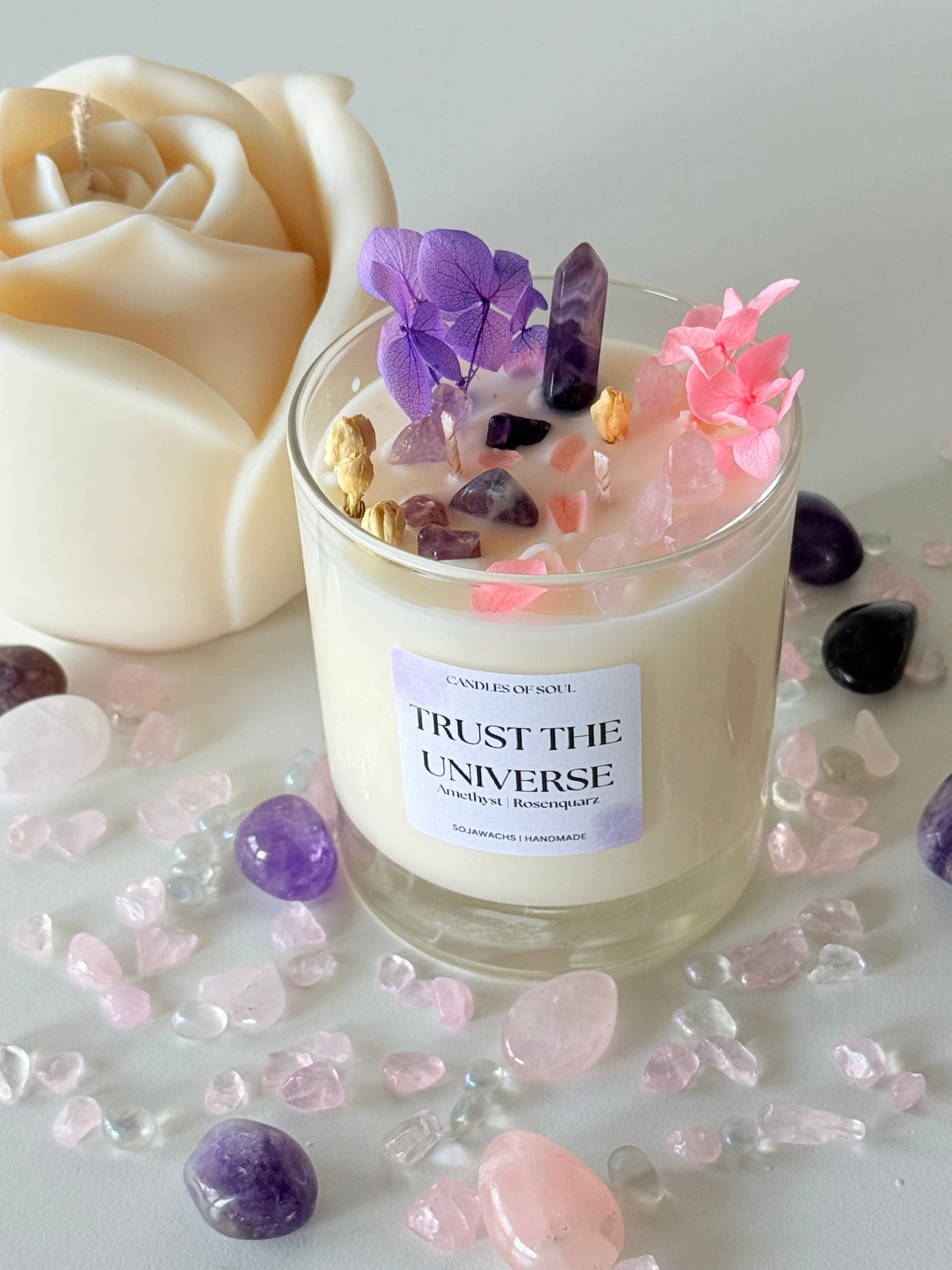 Eine handgefertigte Sojawachskerze im Glas mit der Aufschrift „Trust the Universe“, verziert mit Amethyst- und Rosenquarz-Steinen, getrockneten Blüten in Rosa und Lila sowie kleinen Kräutern. Die Duftkerze strahlt eine spirituelle und beruhigende Atmosphäre aus. Umgeben von Edelsteinen wie Amethyst und Rosenquarz auf einem hellen Untergrund.
Keywords: Duftkerze, Sojawachs, Amethyst, Rosenquarz, Edelsteinkerze, Kristallkerze, Achtsamkeit, Meditation, Spiritualität, Entspannung, Heilsteine, Chakra-Heilung