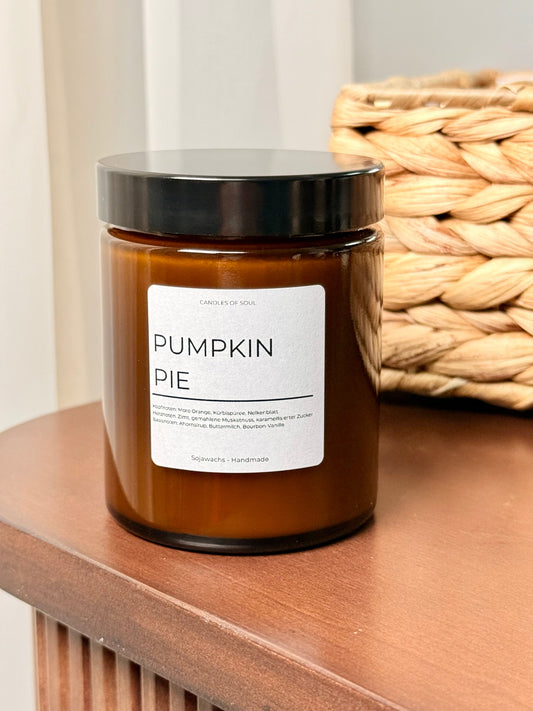 Stimmungsvoll: brennende Kürbis-Duftkerze vor hellem Vorhang.