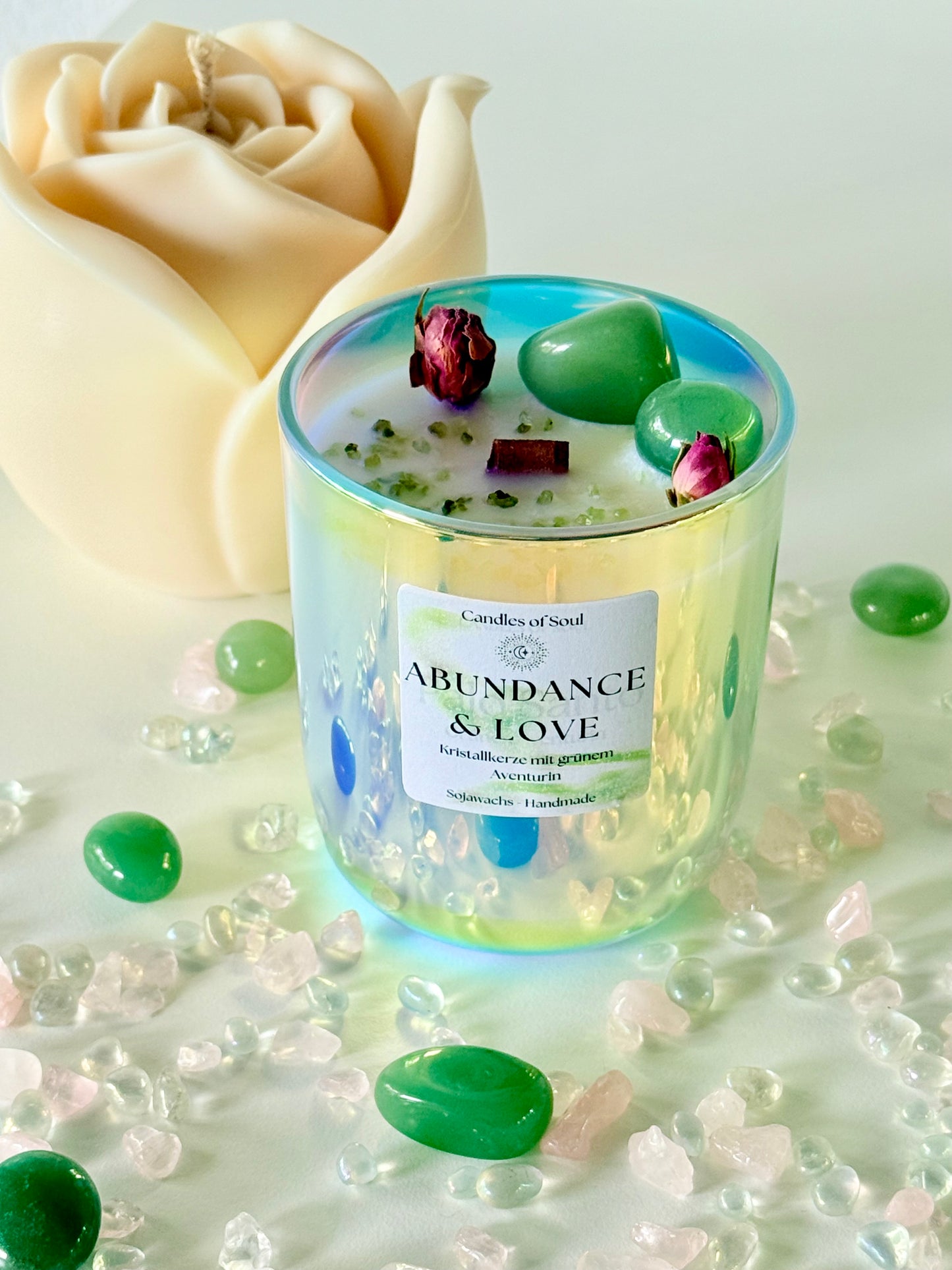 Handgemachte Kristallkerze 'Abundance & Love' mit grünem Aventurin und Rosenknospen auf dekorativem Untergrund.