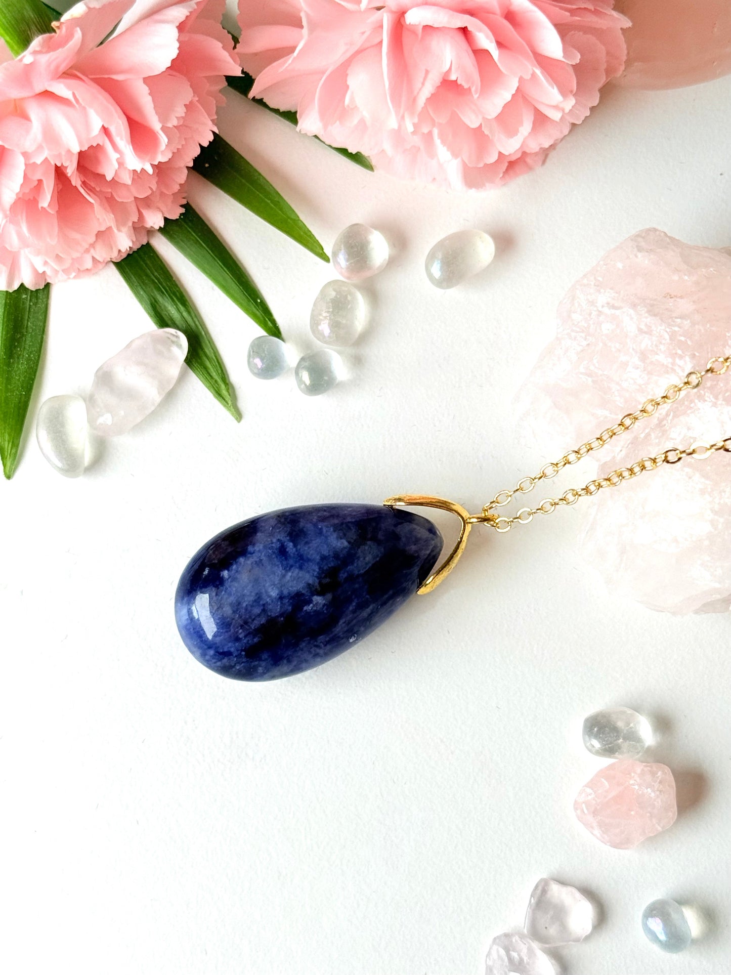 Blauer Sodalith-Tropfenanhänger mit goldfarbener Kette auf rosa Kristallen