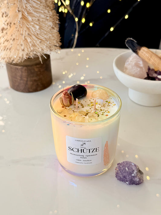 Nahaufnahme einer Sojawachs Kerze mit echten Citrin und Amethyst Steinen sowie getrockneten Blüten.