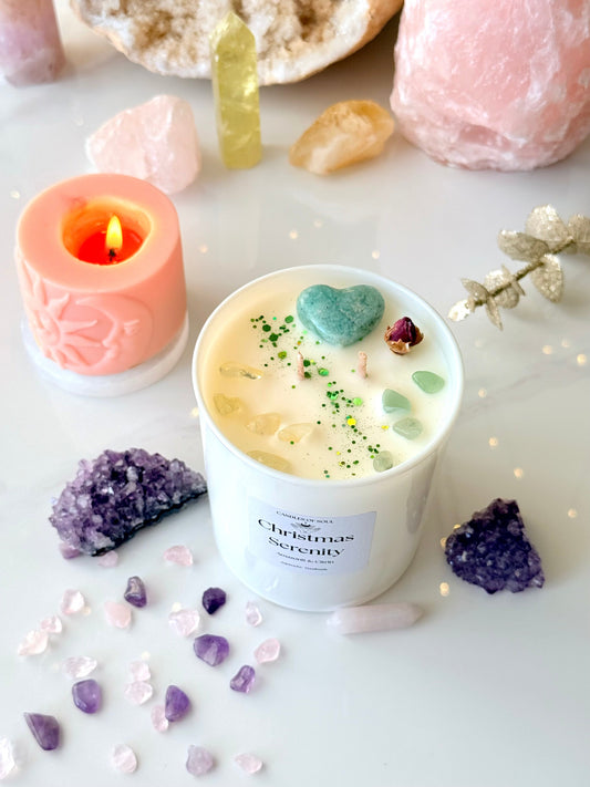 Weiße Sojawachs Duftkerze im Glas mit Label Christmas Serenity, dekoriert mit grünem Amazonit Herz und Citrin Splittern, im Hintergrund weihnachtliche Lichter und Kristalle