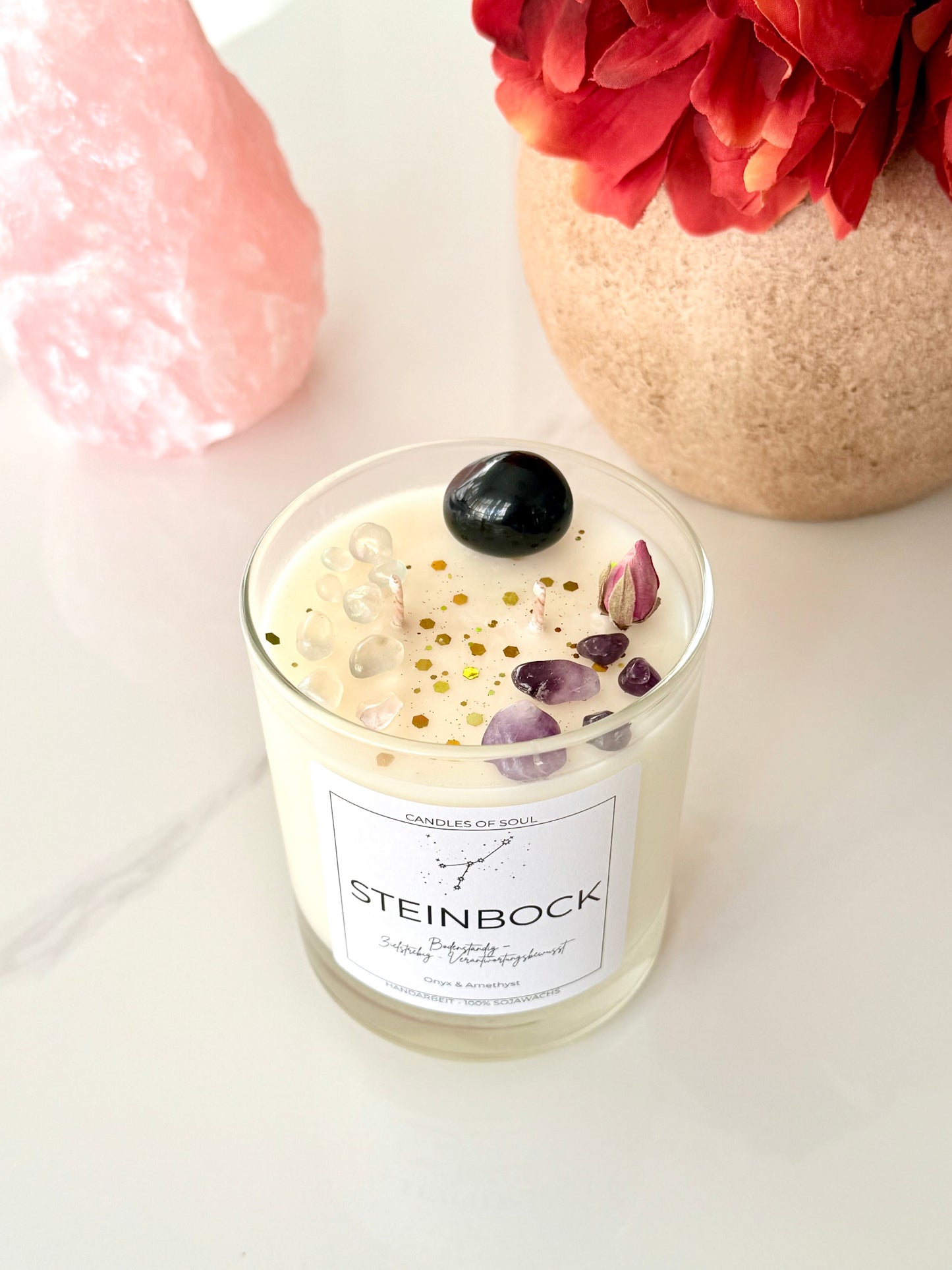Zodiac Candle Capricorn – spirituelle Duftkerze mit Edelsteinen und Blumen-Deko im Hintergrund