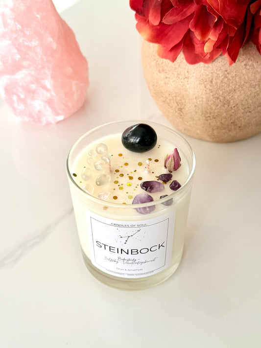 Zodiac Candle Capricorn – spirituelle Duftkerze mit Edelsteinen und Blumen-Deko im Hintergrund