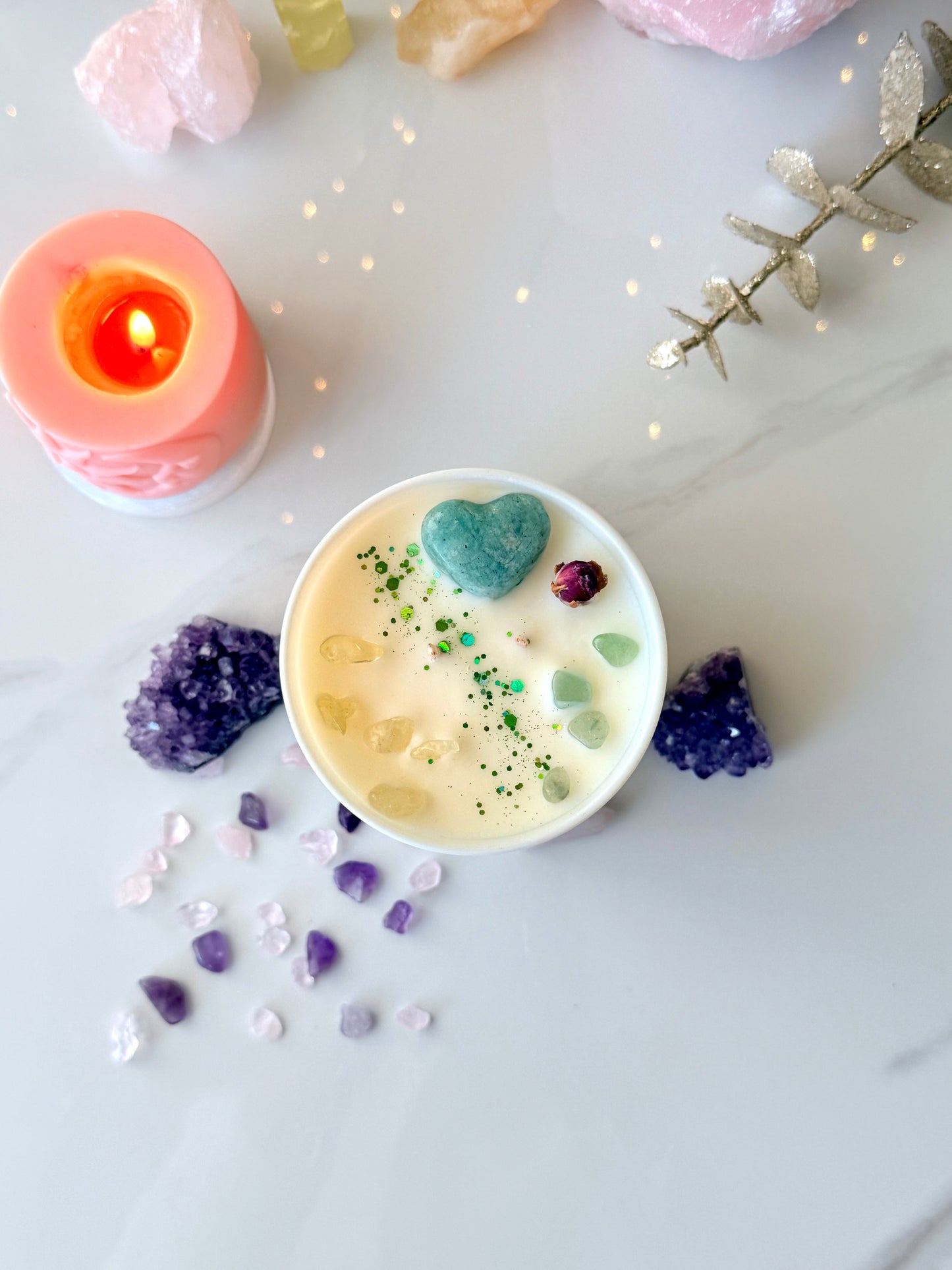 Draufsicht auf handgemachte Kristallkerze, Amazonit Herzstein, gelbe Citrin Edelsteine und getrocknete Rosenknospe auf cremeweißem Sojawachs, spirituelle Deko