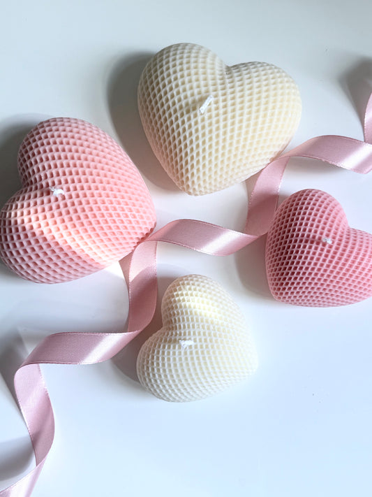 Herzförmige Kerzen in Rosa und Creme mit 3D-Waffelstruktur auf weißem Hintergrund, dekoriert mit rosa Satinband.
