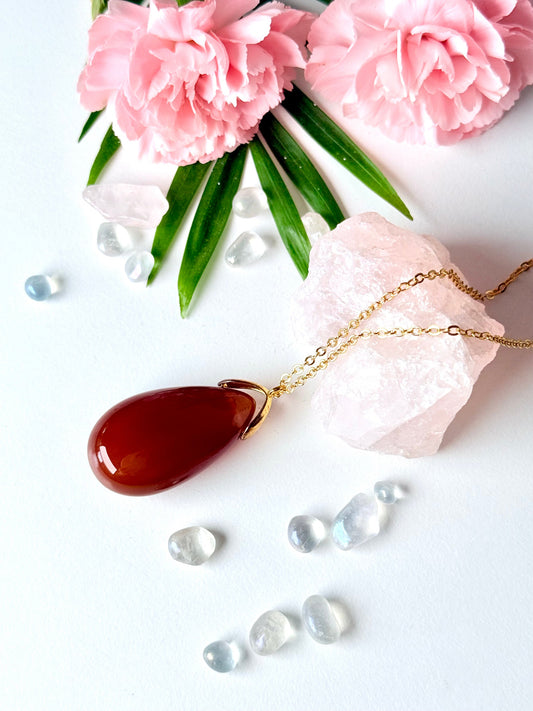 Karneol Tropfenanhänger mit vergoldeter Kette auf rosa Kristallen und Blumen