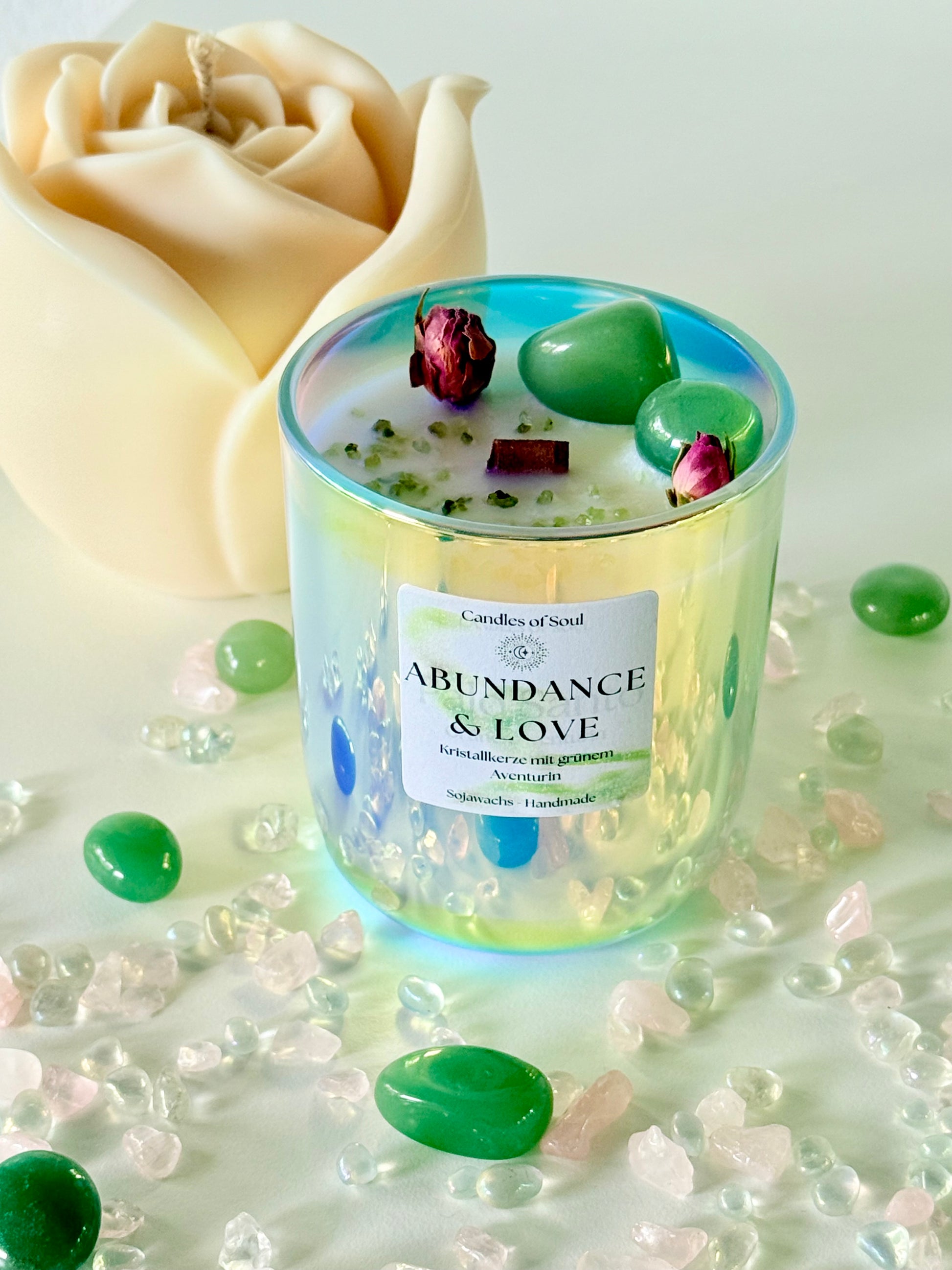 Handgemachte Kristallkerze 'Abundance & Love' mit grünem Aventurin und Rosenknospen auf dekorativem Untergrund.