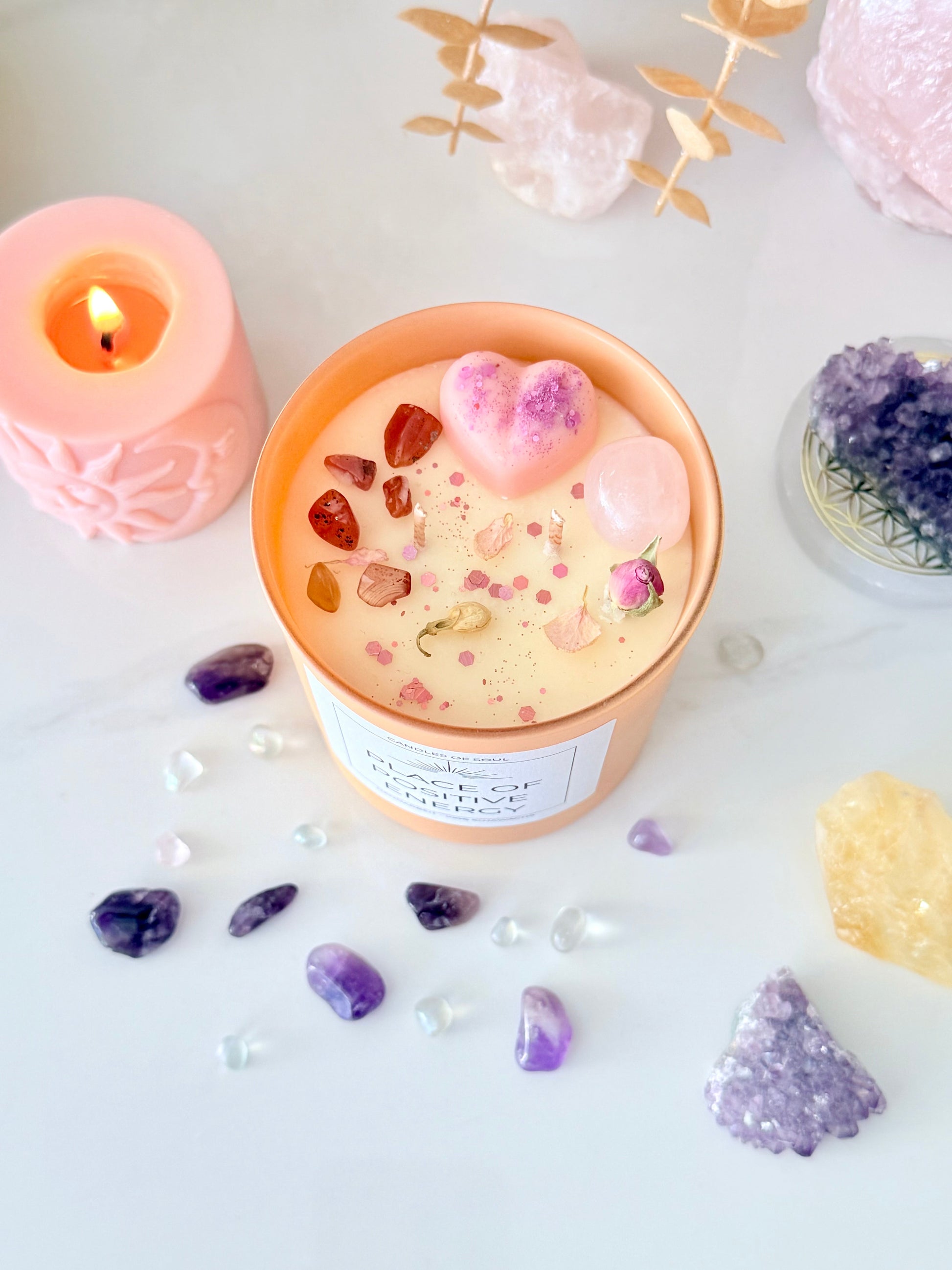 Orange Kerze für positive Energie, dekoriert mit Rosenquarz, Karneol und Blüten.