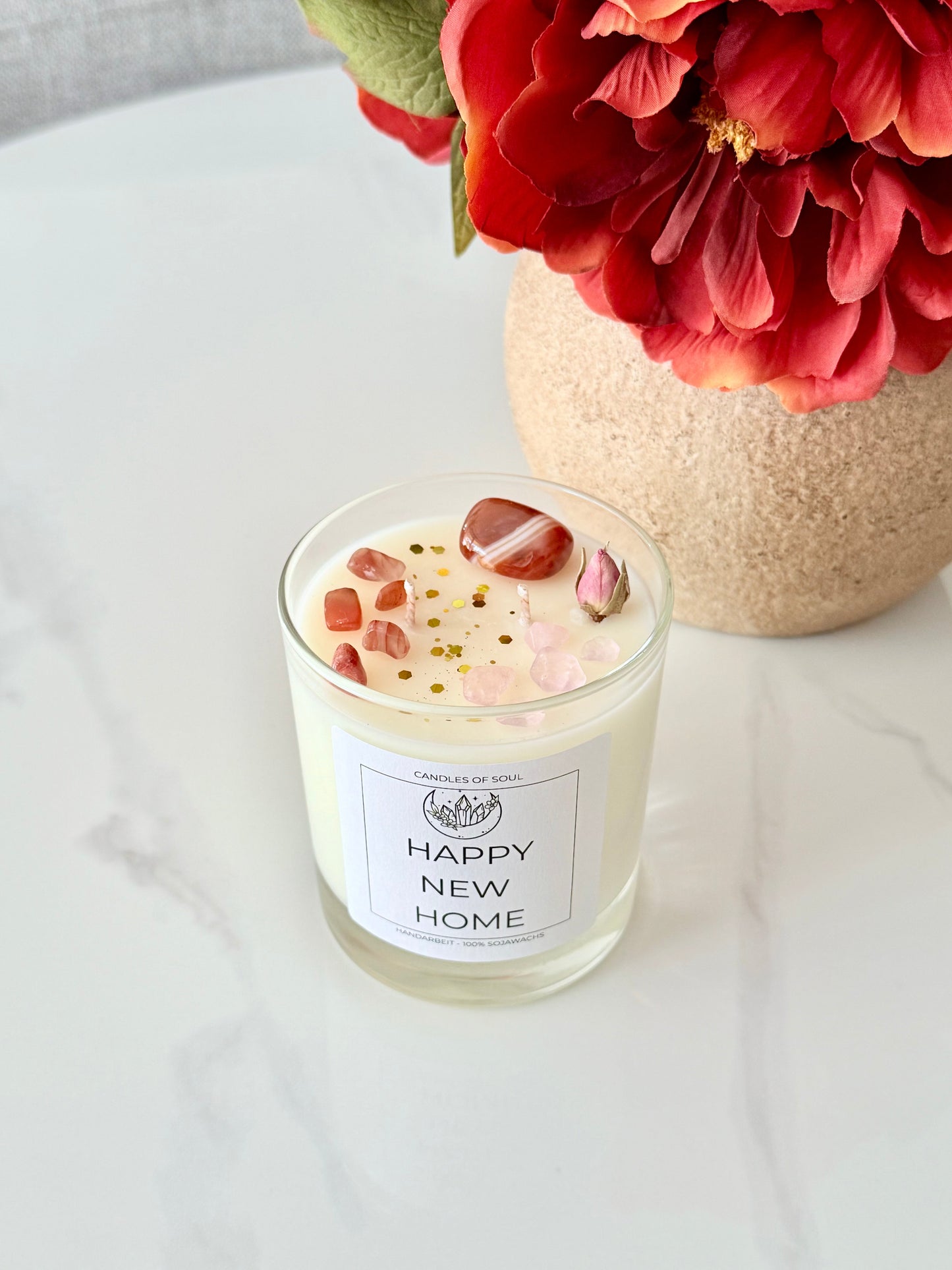 Spirituelle Duftkerze mit Edelsteinen und Blütendekor auf hellem Marmortisch.