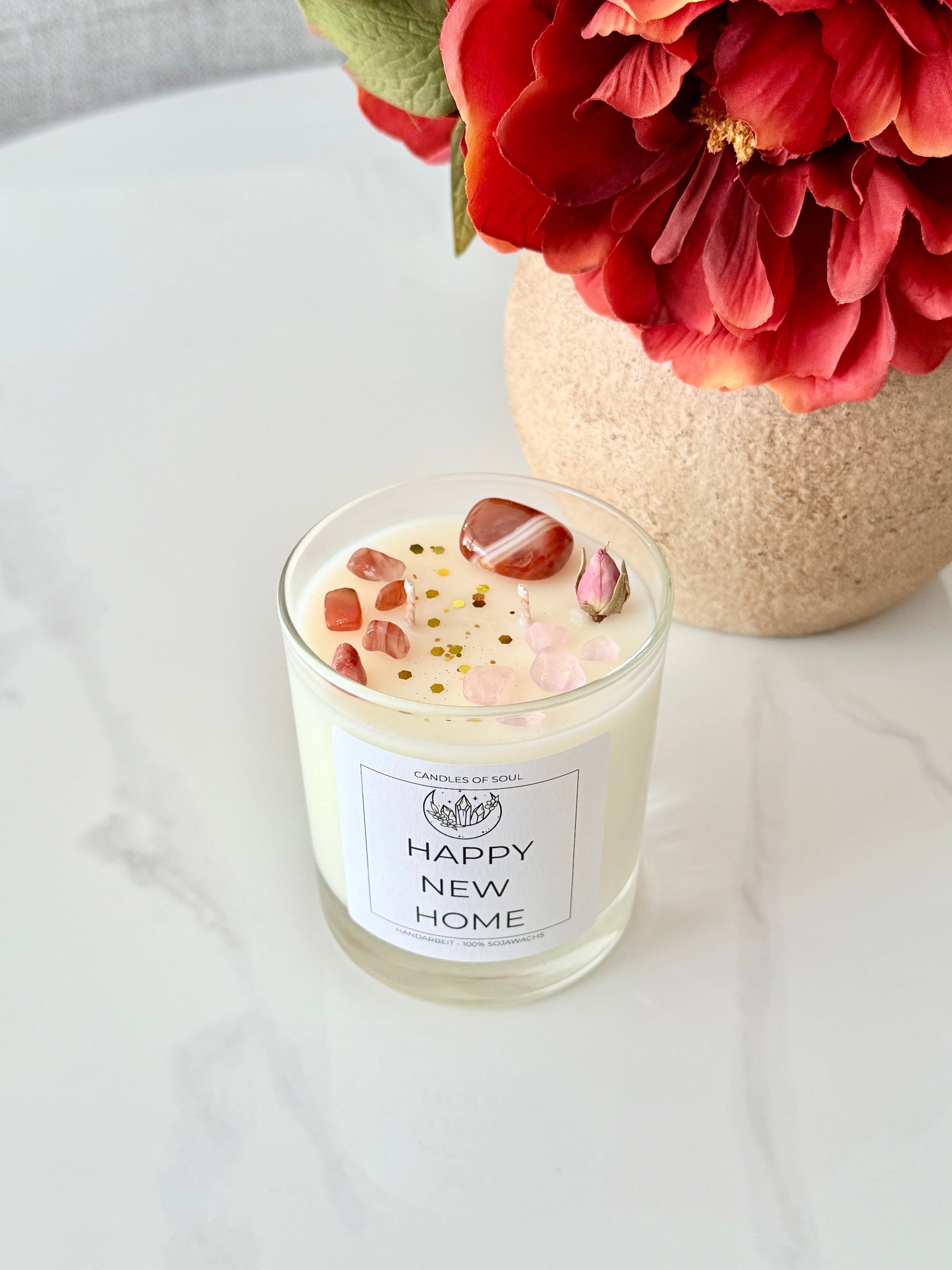 Spirituelle Duftkerze mit Edelsteinen und Blütendekor auf hellem Marmortisch.