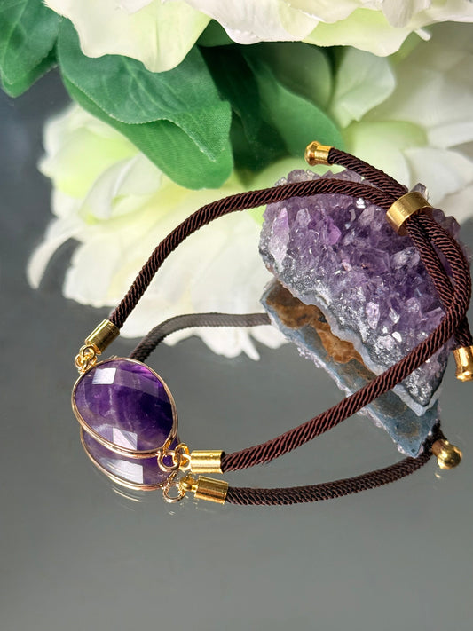 Detailansicht des facettierten Amethyst-Steins in Tropfenform, eingefasst in nickelfreies Gold an dunkler Kordel.