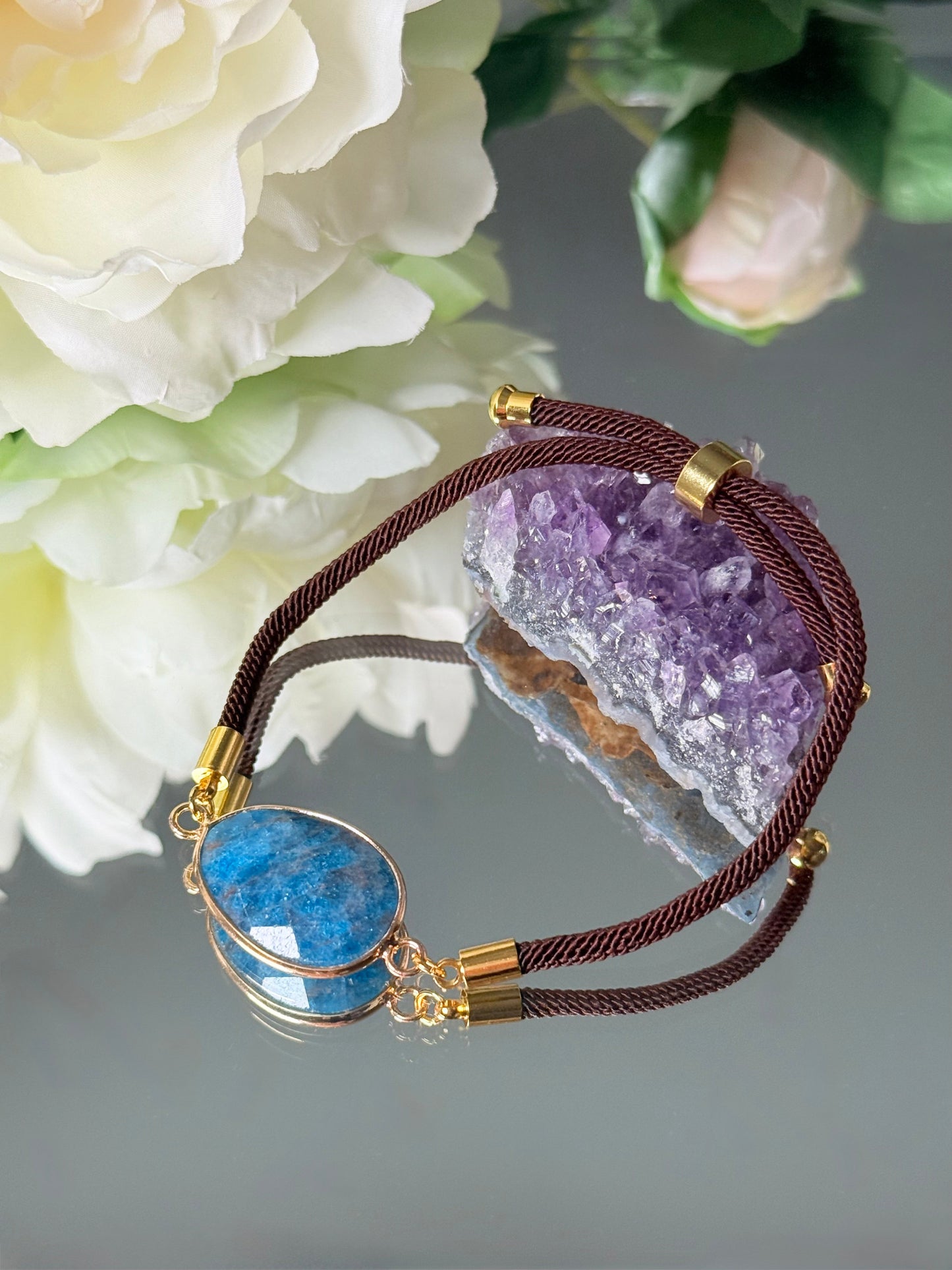 Verstellbares Armband aus echtem blauen Apatit mit goldenen Details, liegend auf hellem Untergrund.