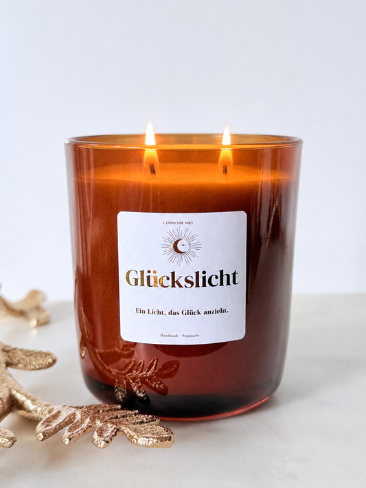 Glückslicht Duftkerze aus Sojawachs im braunen Glas mit weißem Etikett und dem Motto Ein Licht, das Glück anzieht
