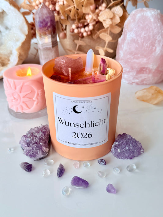 Apricotfarbene Kristallkerze im Glas mit Label Wunschlicht 2026, dekoriert mit Rosenquarz und Amethyst Clustern.