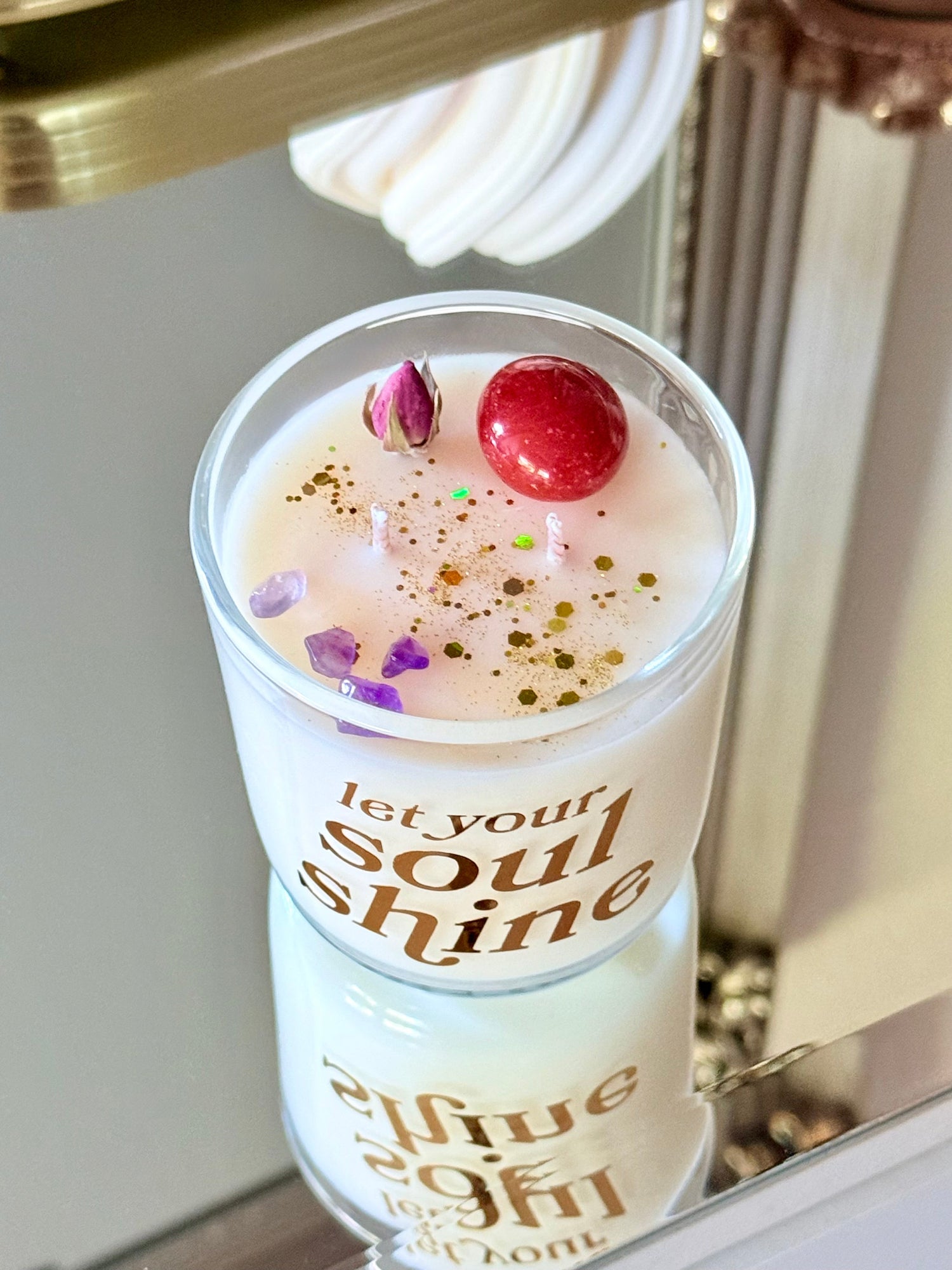 Nahaufnahme der Let Your Soul Shine Kerze mit Gold-Aufdruck und Rosenblüte.