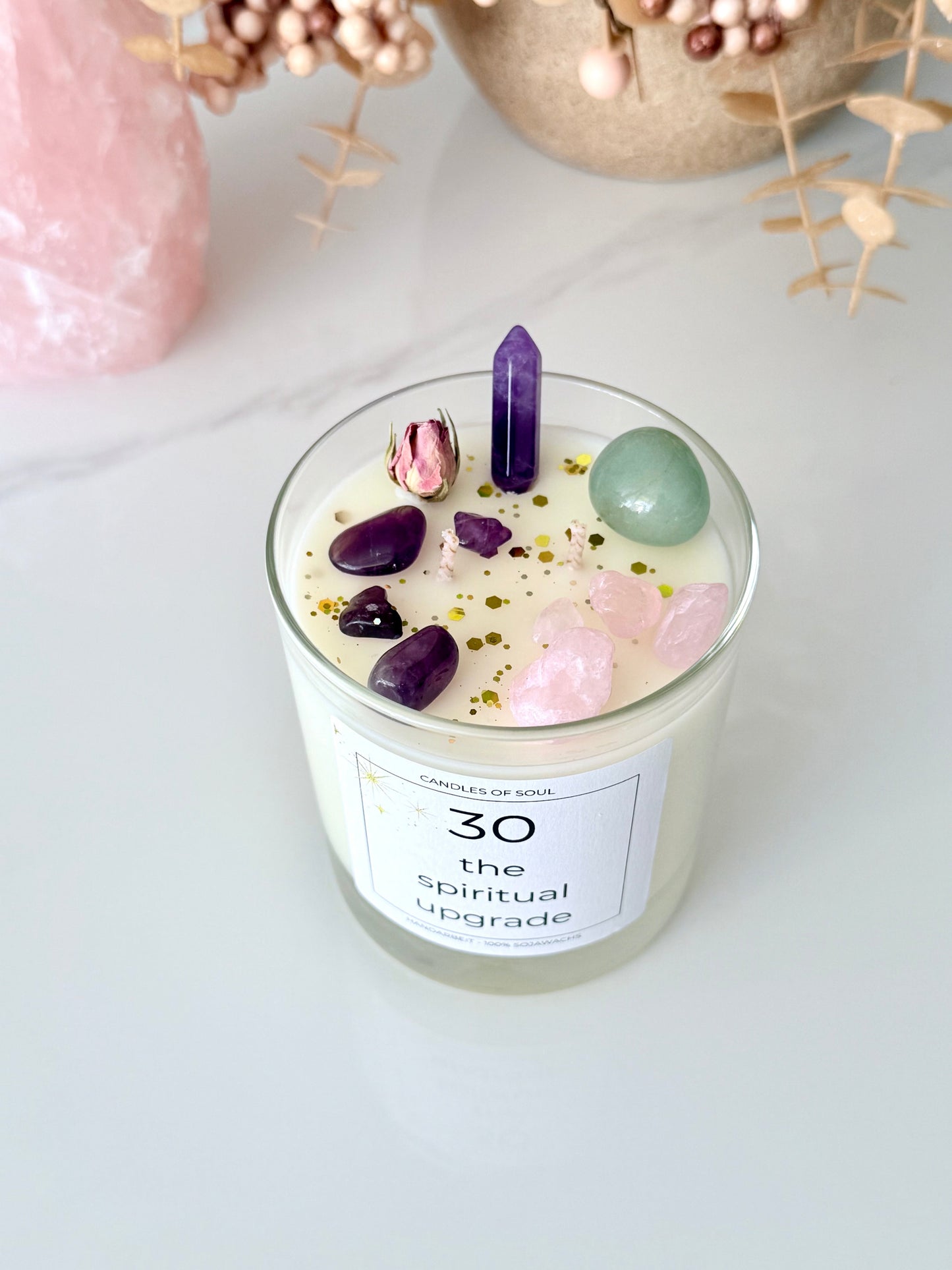 Spirituelle Duftkerze mit Edelsteinen und getrockneter Rose auf weißem Hintergrund.