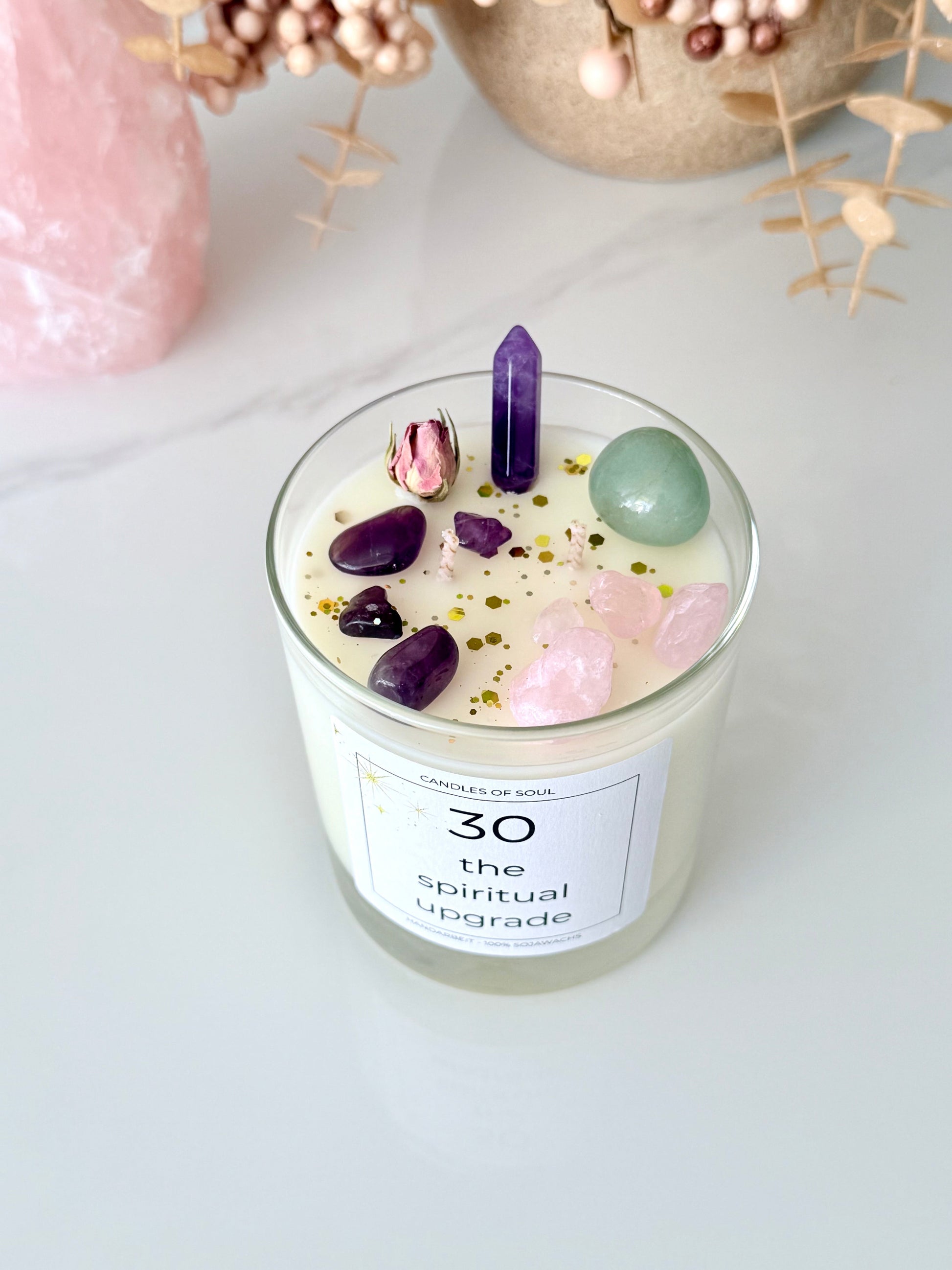 Spirituelle Duftkerze mit Edelsteinen und getrockneter Rose auf weißem Hintergrund.