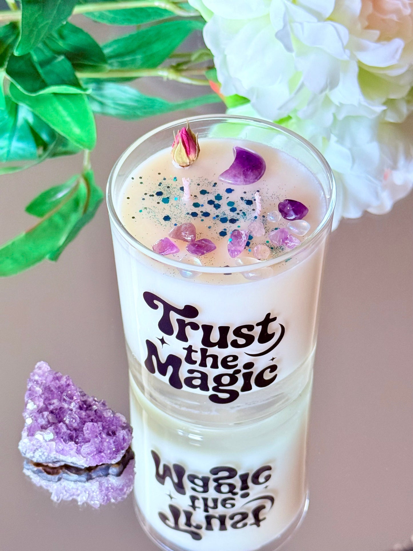 orderansicht der Sojawachskerze im Glas mit dem schwarzen Retro-Schriftzug "Trust the Magic", dekoriert mit einem Amethyst-Mond, Heilsteinen und blauem Glitzer.