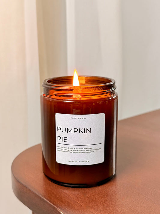 Brennende Pumpkin Pie Duftkerze im bernsteinfarbenen Glas auf Holztisch.